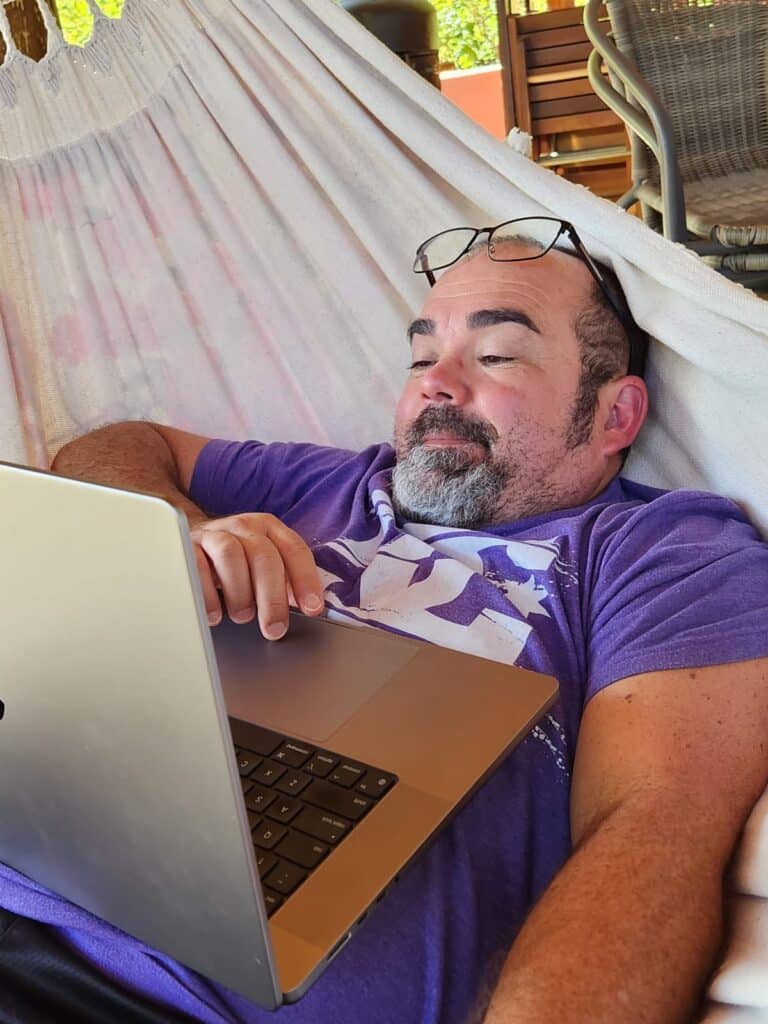 Roger lounging in a hammock, working on Shades In Place on his laptop