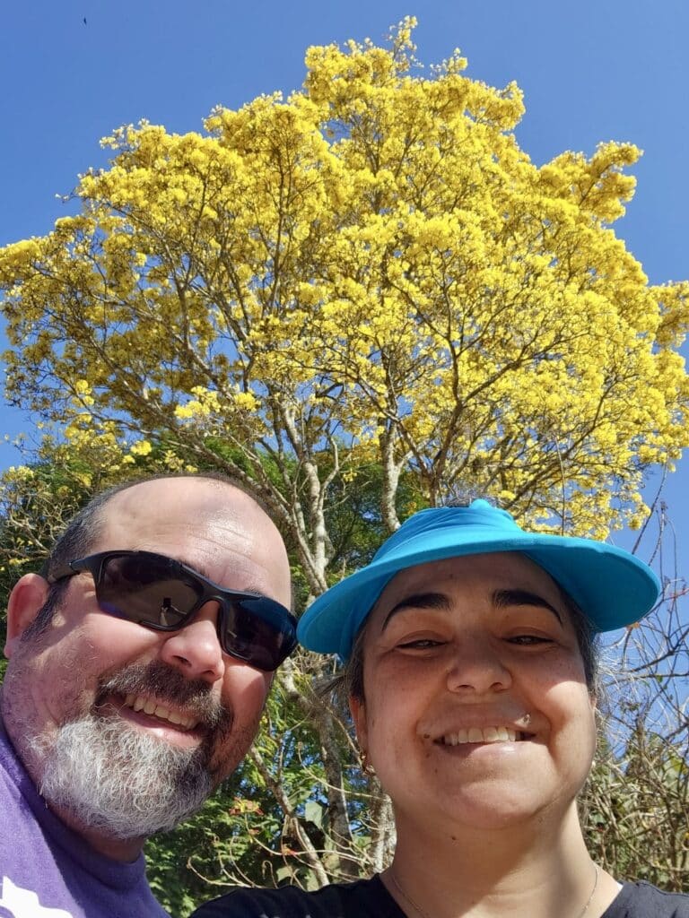 Roger Magalhaes, window treatments installer, posing with his sister in front of a tree with yellow leaves