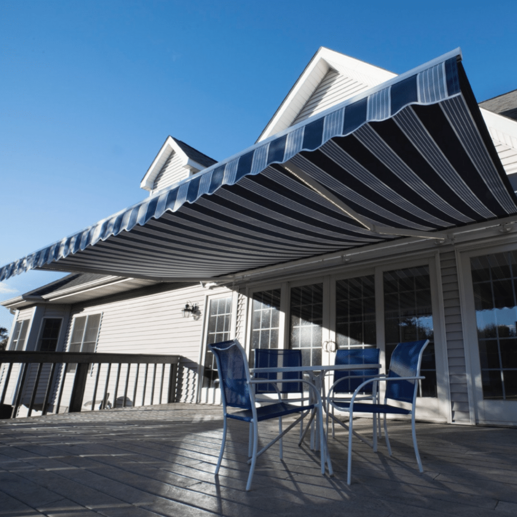 Back of a house featuring a retractable blue and white striped awning, outdoor window treatment providing shade and style to the space.