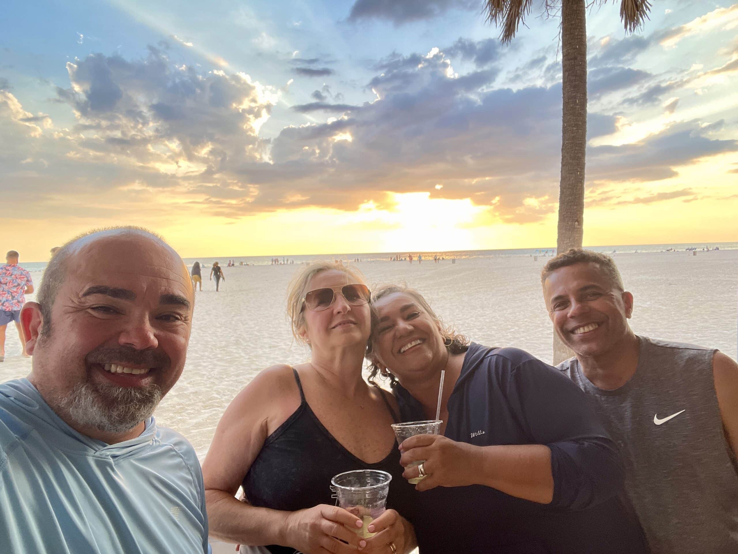 Roger and Ana Magalhaes posing with friends on the beach, with a stunning sunset in the background