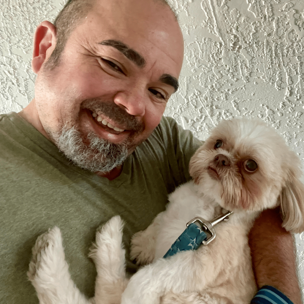 "Roger Magalhaes, motorized window treatments installer, smiling while holding a playful dog.