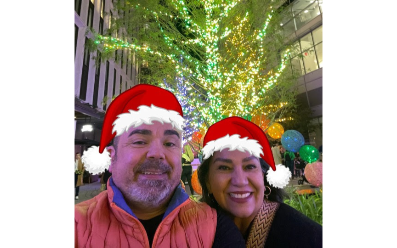 Roger and Ana Magalhaes smiling in a festive selfie, both wearing Christmas hats, capturing the holiday spirit.