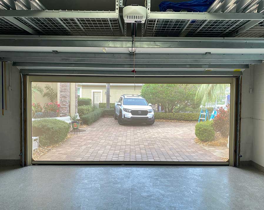 From inside garge door looking through a screen with car parked on brick driveway